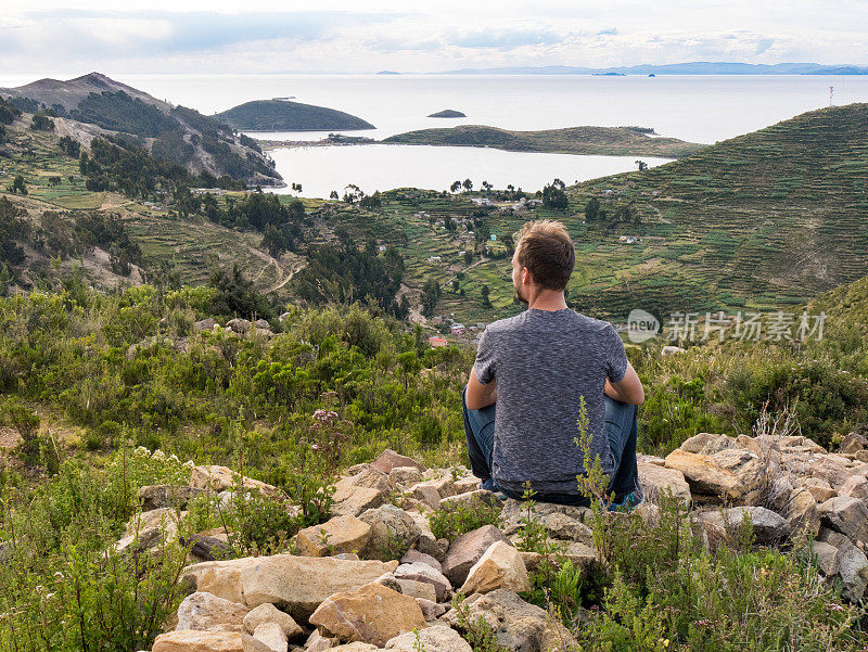 玻利维亚科帕卡巴纳，阳光岛，titicaca isla del sol湖，年轻的白人男性坐在欣赏美丽的风景山丘，山脉